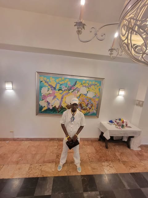 Man dressed all in white in front of a colorful painting